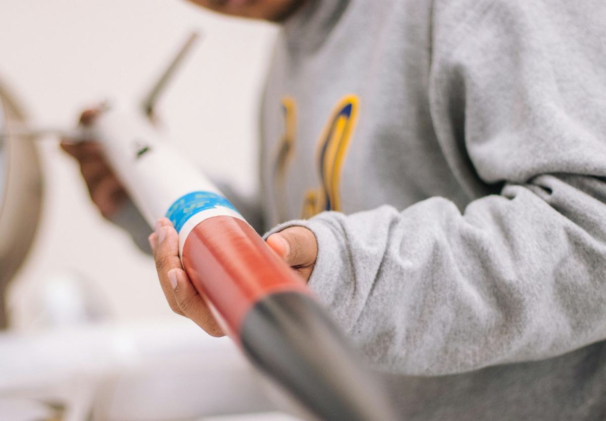 Hands holding a caulk gun fitted with a cartridge.