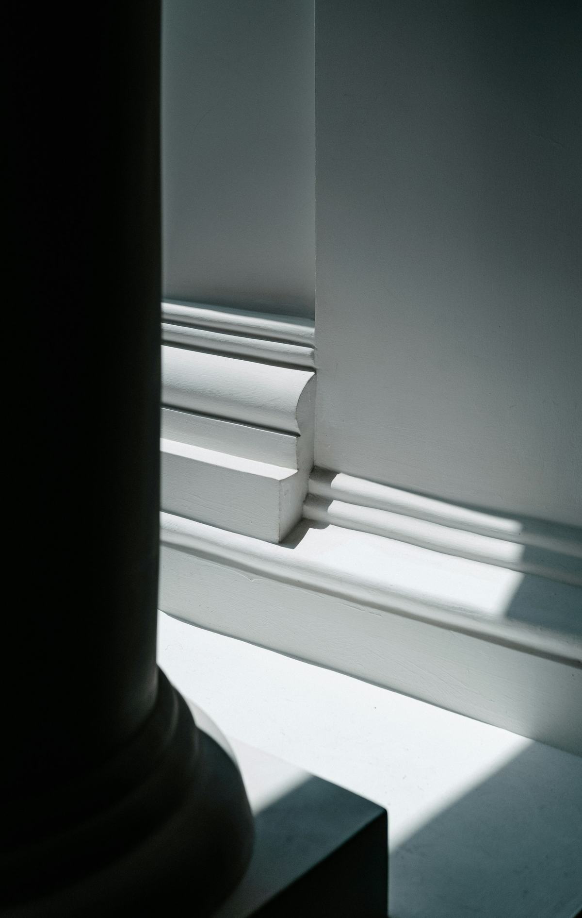 Close view of a stepped white baseboard profile at the base of a column.