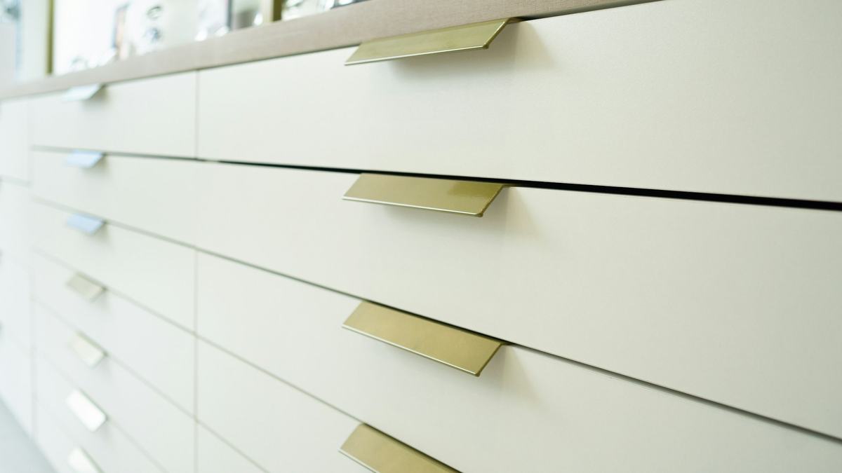 Row of flat cream drawer fronts with brass edge pulls.