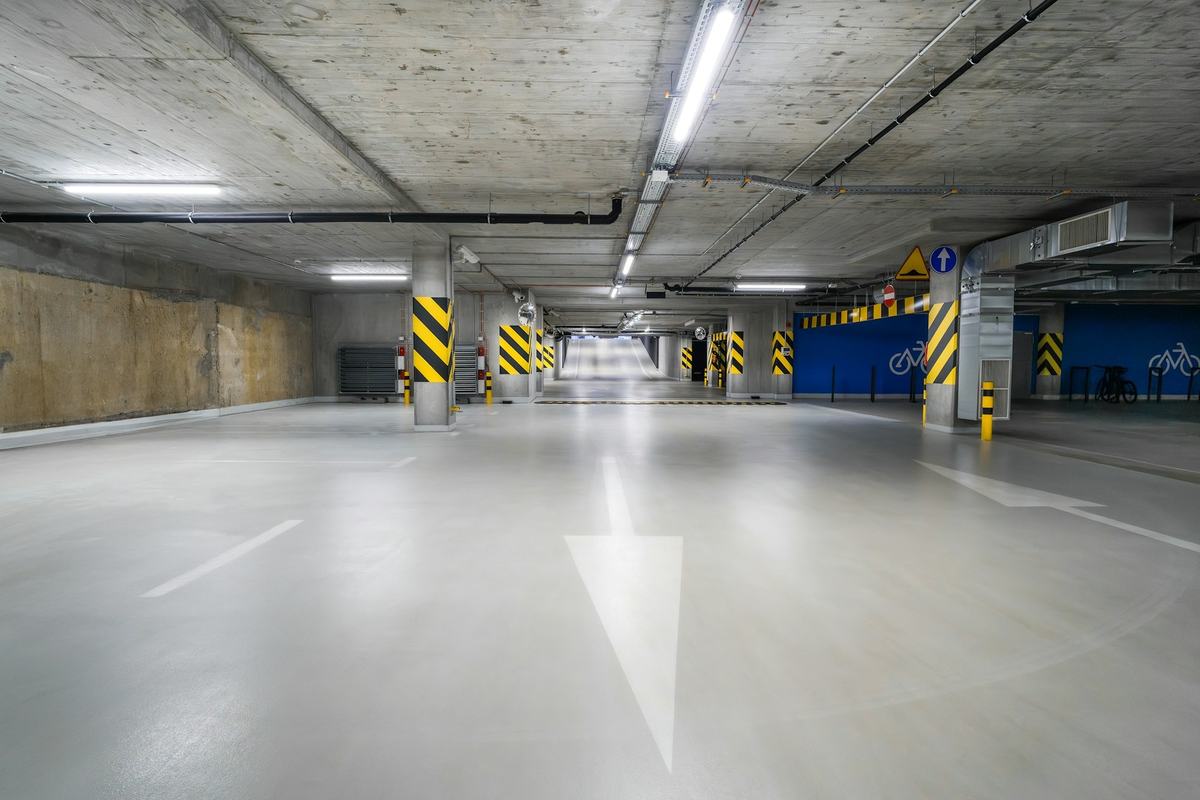 Parking structure with a smooth gray coated floor reflecting overhead lights.