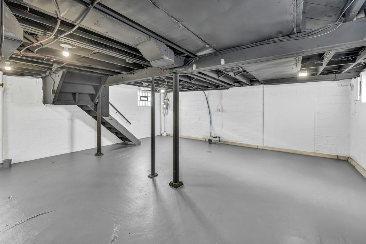 Black-and-white photo of a basement-level space with a uniform solid-color coated floor and steel posts.