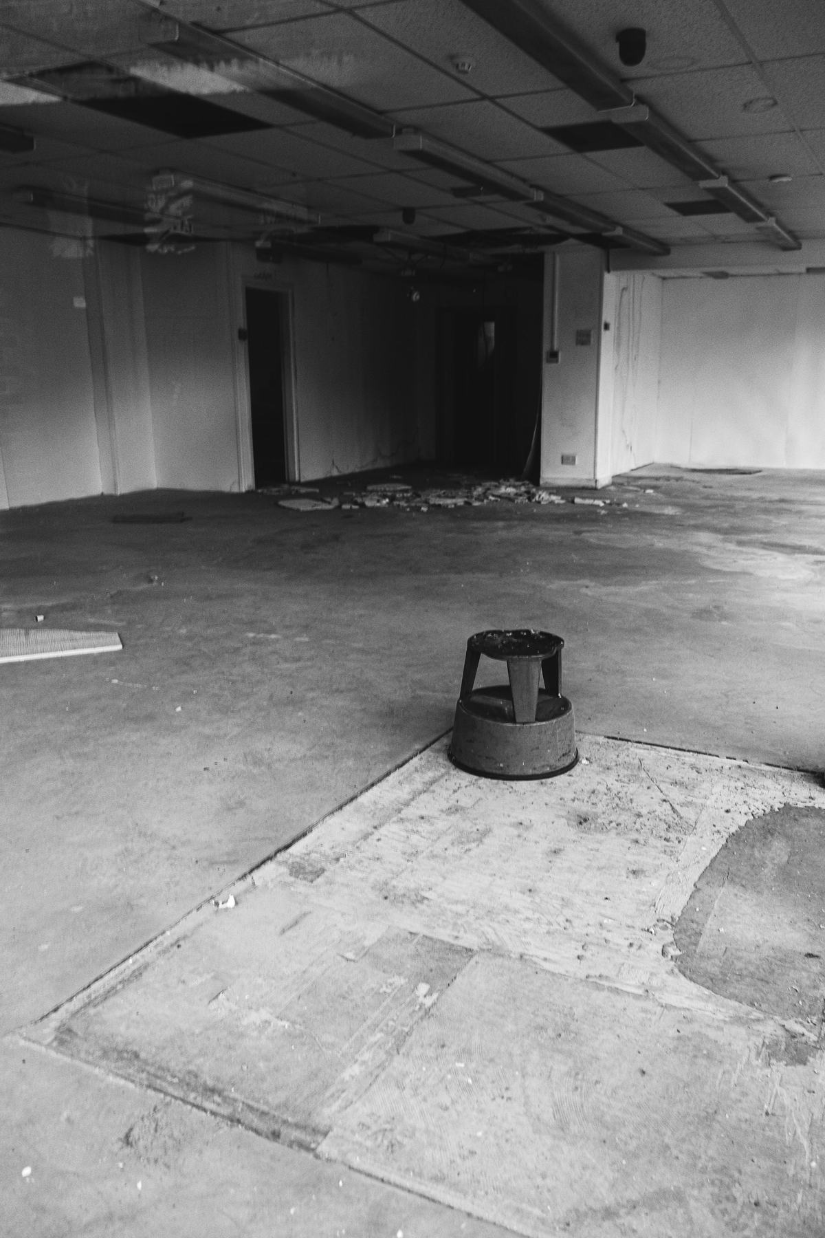 Black-and-white photo of an empty interior with a bare concrete slab showing patches and old adhesive lines.