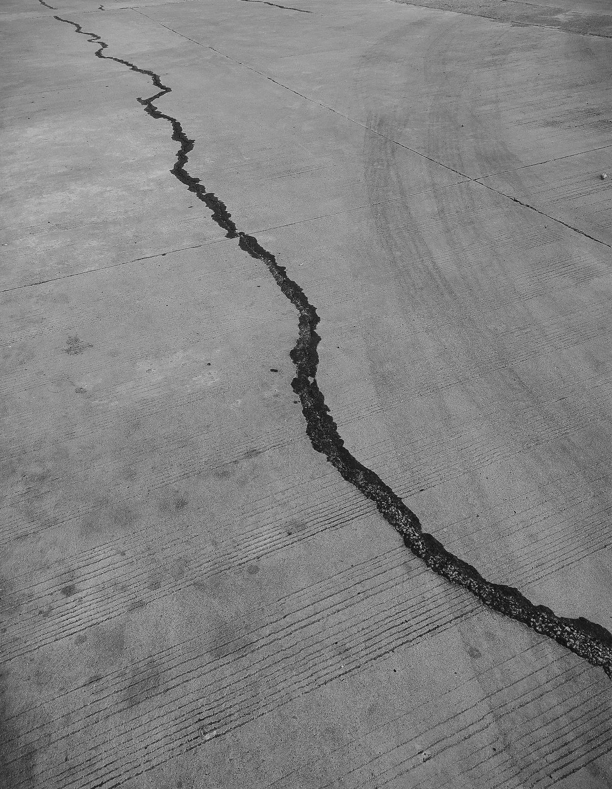 Black-and-white photo of a crack running across a broom-finished concrete slab.