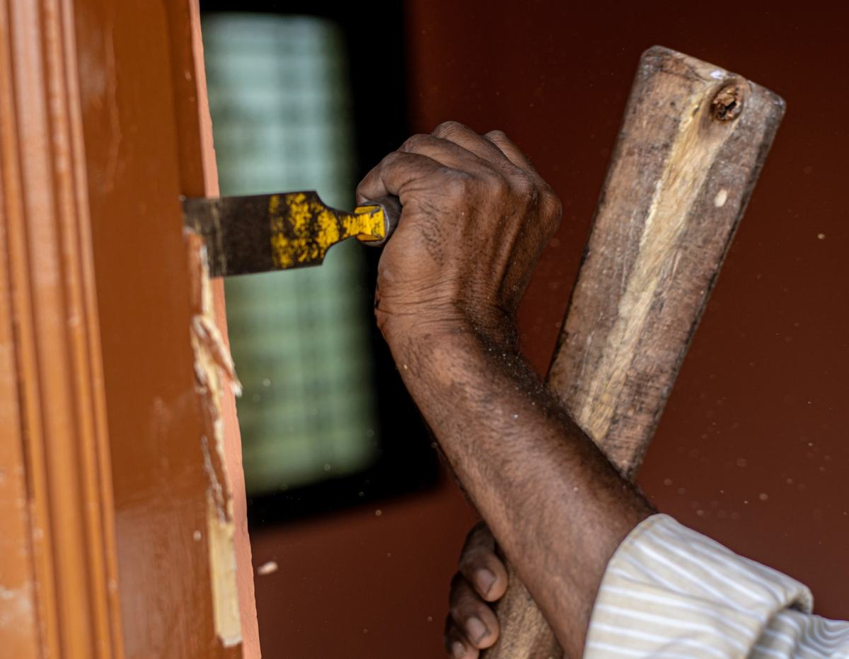 Hand using a chisel and mallet on a door frame.