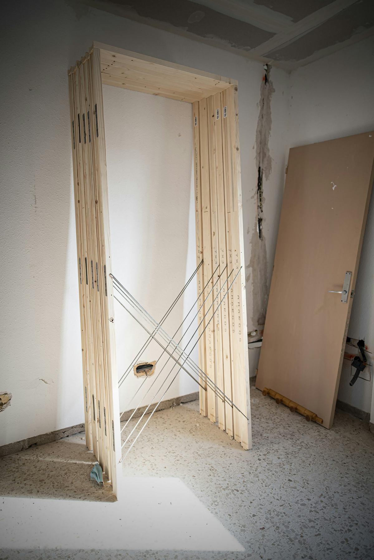 Door frame assembly standing in a room under renovation with a door slab leaning against the wall.