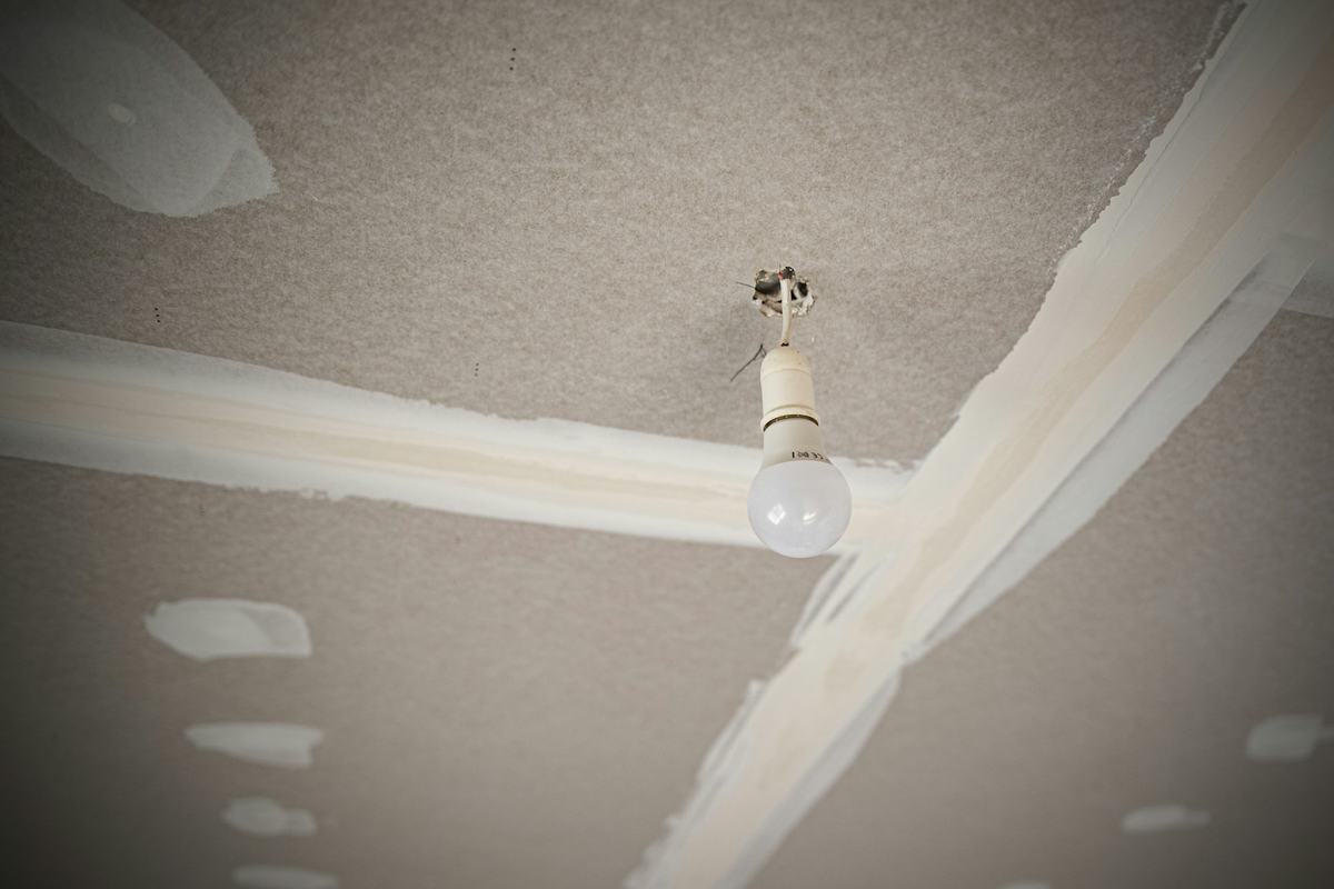 Ceiling drywall with taped joints and spots of joint compound around a bare bulb.