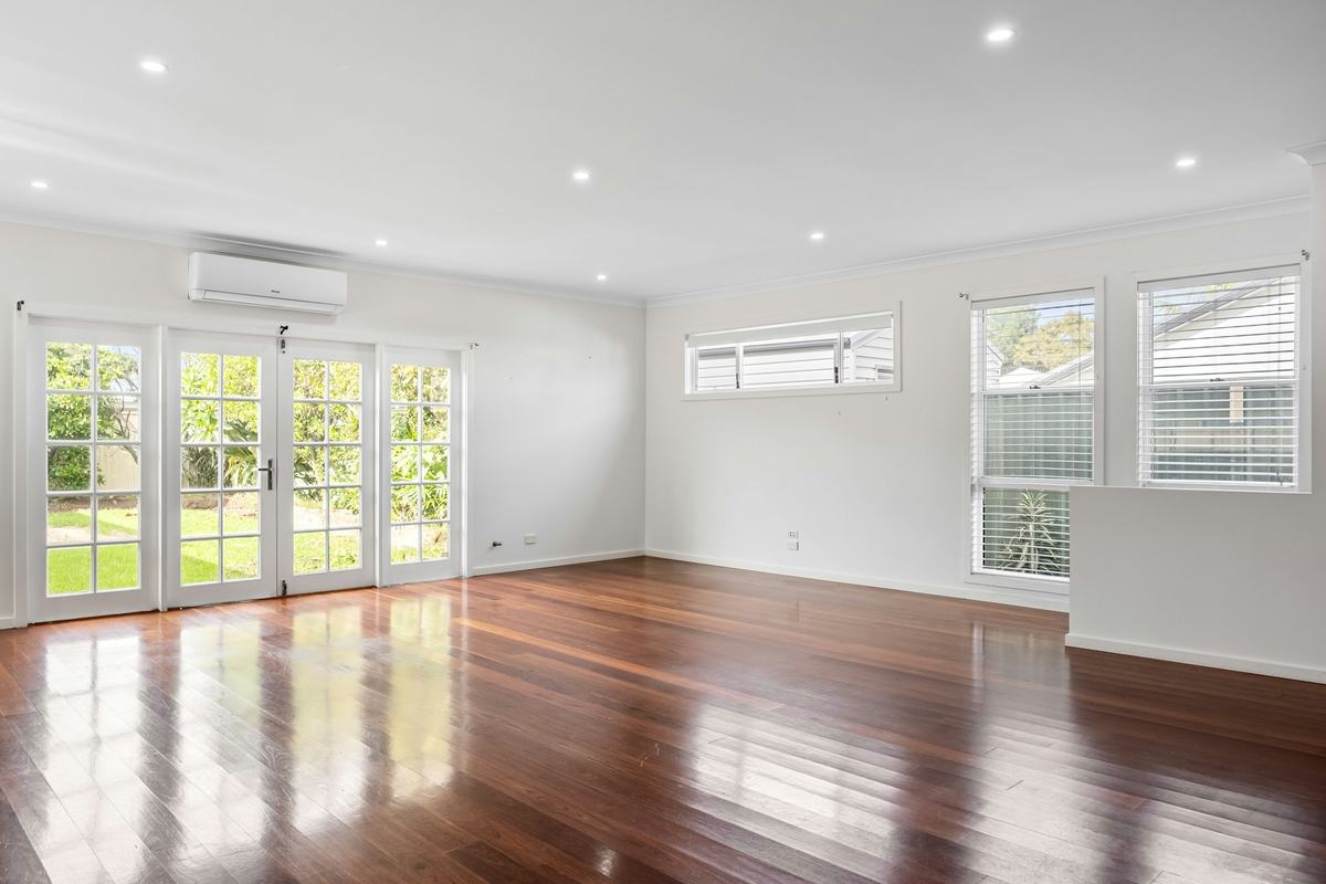Empty living room with white walls, white ceiling and glossy wood flooring.