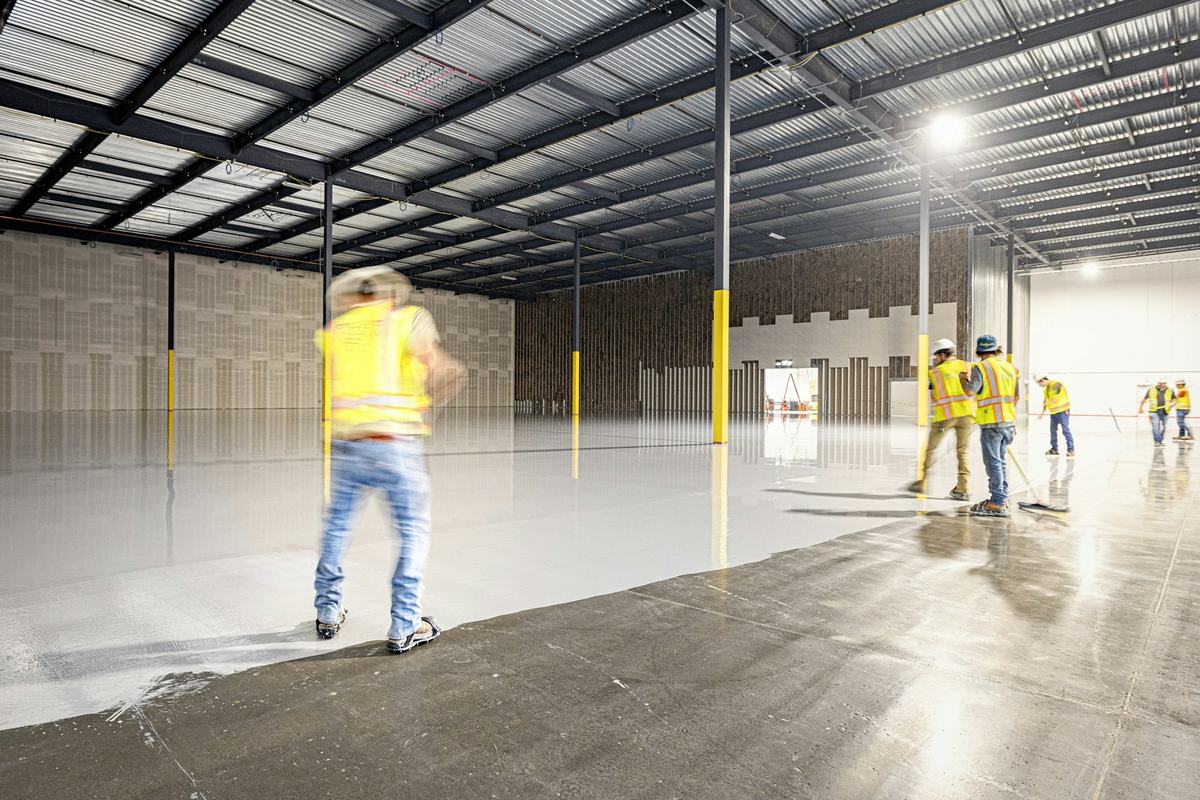 Crew applying a light-colored floor coating across a large concrete floor.