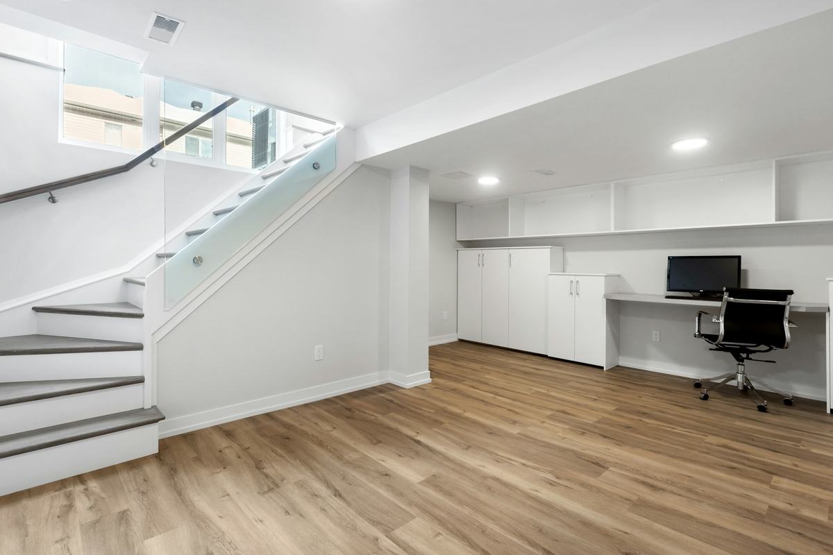 Finished lower level with plank flooring, white walls, a staircase and built-in cabinets.