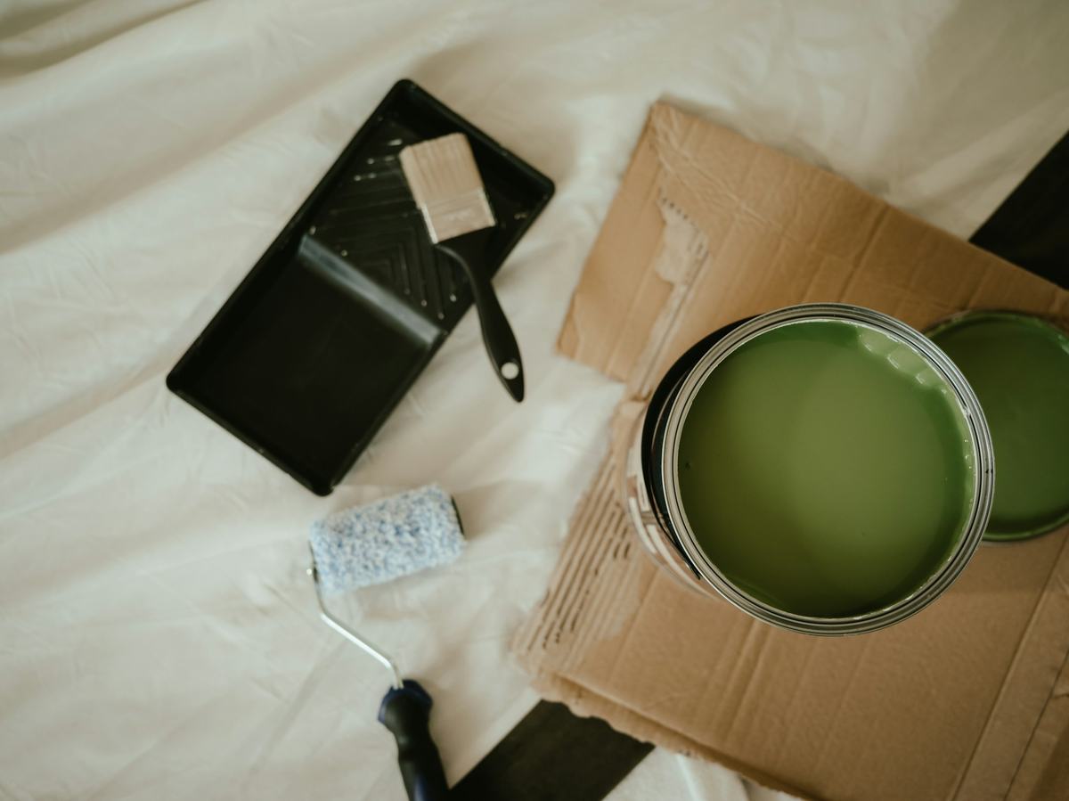 Paint can, roller and tray set out on a canvas drop cloth, seen from above.