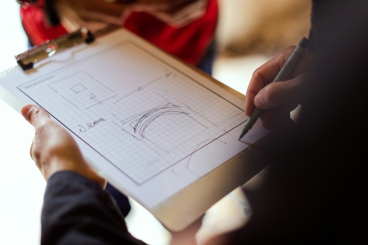 Hands sketching a plan on a clipboard.